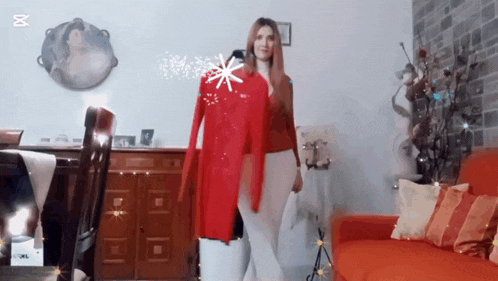 a woman is standing in a living room holding a red sweater