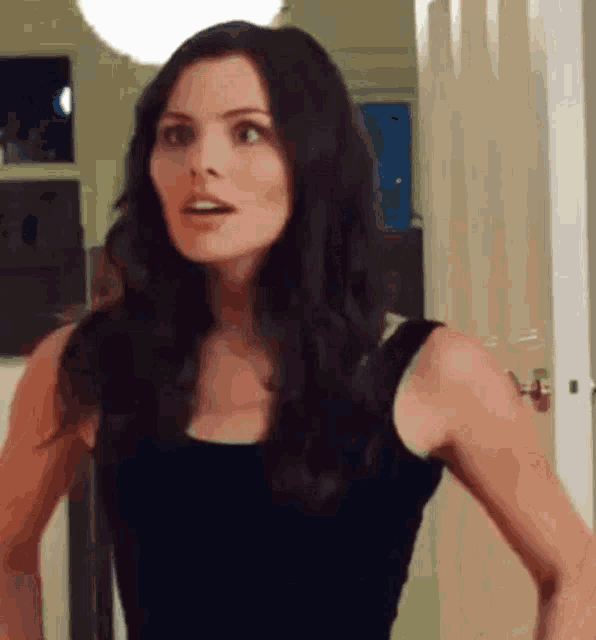 a woman in a black tank top stands in front of a door