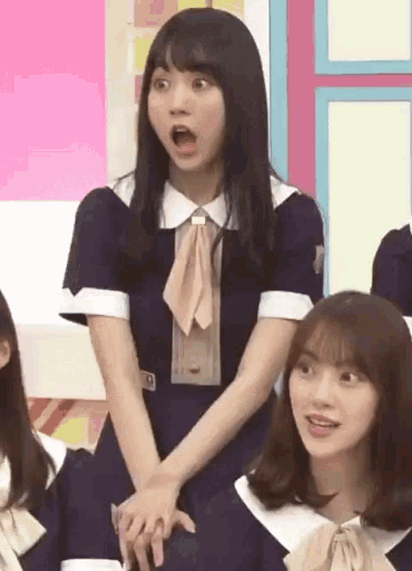 a group of girls are sitting in a room with their hands on their hips and one girl is making a surprised face .