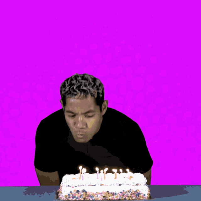 a man is blowing out candles on a birthday cake with the word happy behind him