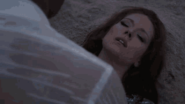 a woman is laying on the beach with her eyes closed and a man is holding her .