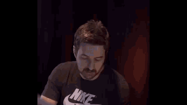 a man with a beard wearing a black nike t-shirt is pointing at something .