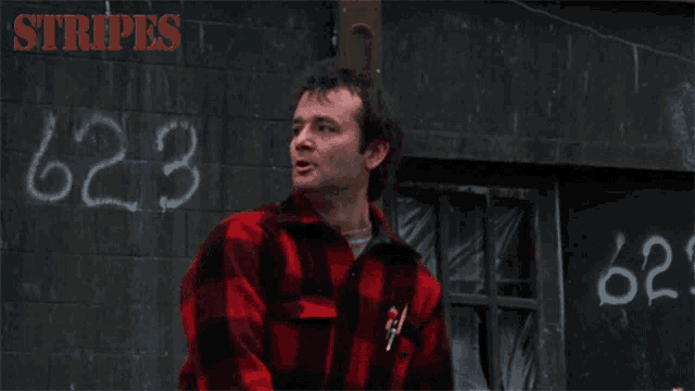a man in a red and black plaid shirt is standing in front of a wall with the number 624 written on it