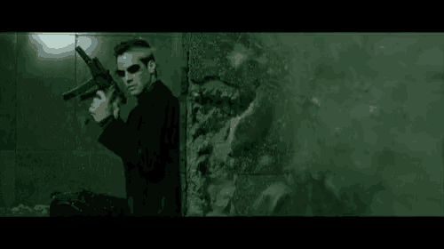 a man in a suit is holding a gun in front of a green wall .