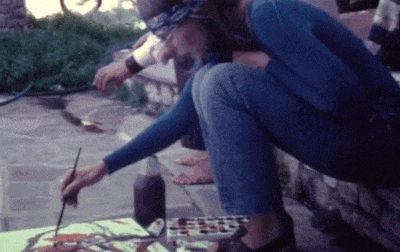 a woman in a blue shirt is kneeling down and painting on a canvas
