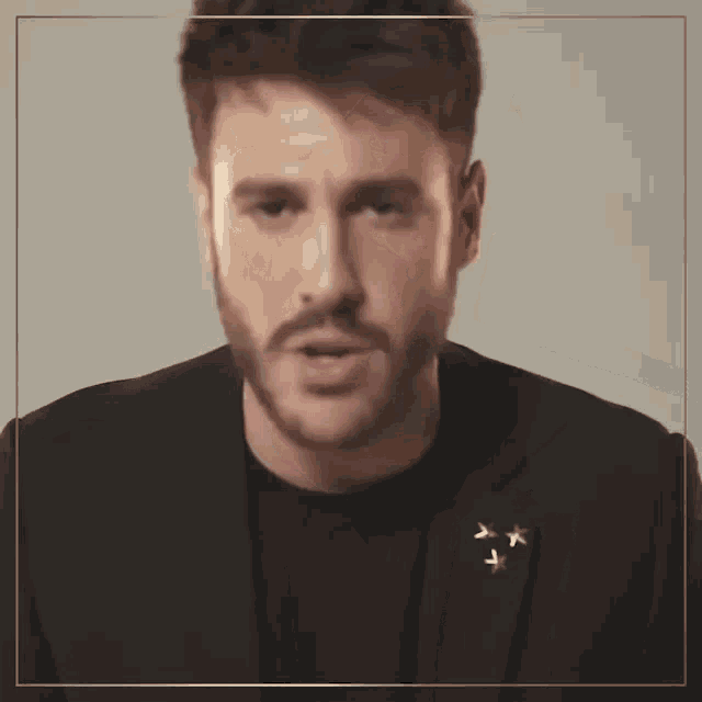 a man with a beard is wearing a black jacket with gold stars on it