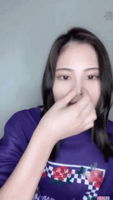 a woman wearing a purple shirt that says akb covers her nose