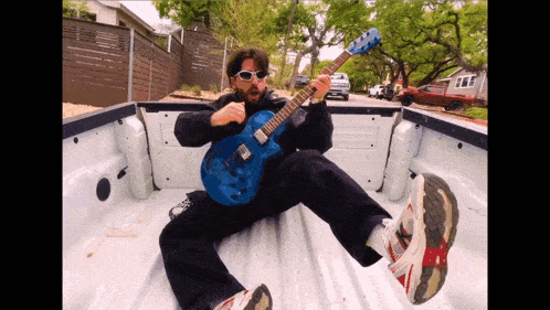 a man wearing sunglasses is playing a blue guitar in the back of a truck
