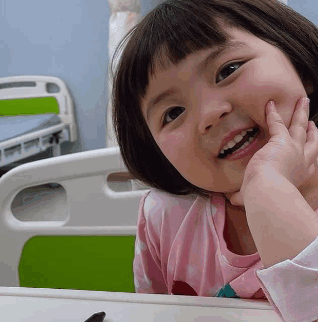 a little girl sitting in a hospital bed with her hand on her face