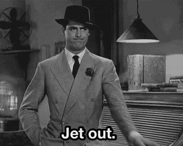 a man in a suit and hat is standing in a room with his hands on his hips and says `` jet out '' .
