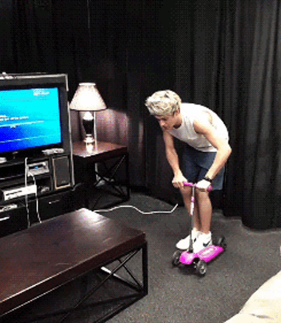 a man riding a pink scooter in front of a tv