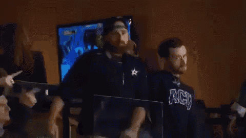a man wearing a black shirt that says ' nbc ' on it stands in front of a television