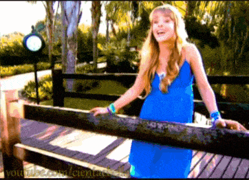 a girl in a blue dress is standing next to a wooden fence