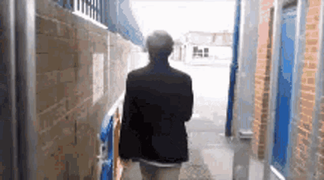 a man in a black jacket is walking down a narrow alleyway .