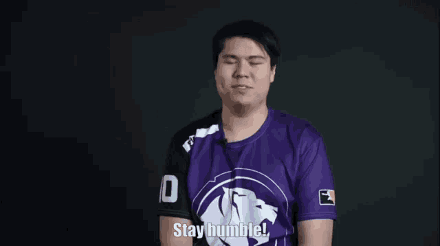 a man in a purple shirt is making a face and says stay humble .