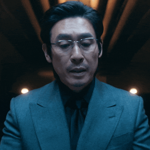 a man wearing glasses and a suit looks at the camera