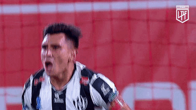 a soccer player in a black and white striped jersey is celebrating a goal on a red field .