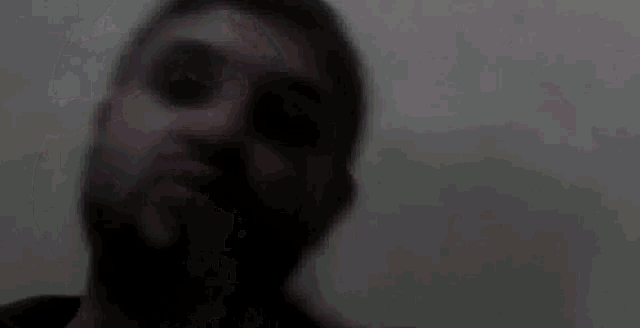 a man with a beard is looking at the camera with a blurry background .