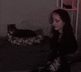 a woman sits next to a cat in a floral bed