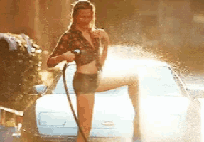 a woman is standing next to a car spraying water on it