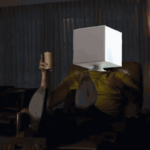 a man with a box on his head holds a cup of coffee