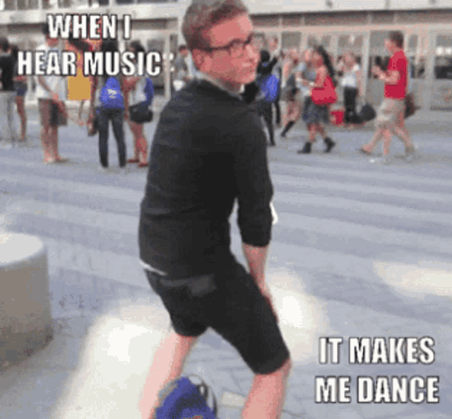 a man in a black shirt and shorts is standing on a sidewalk with a caption that says " when i hear music "