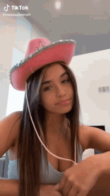 a woman is wearing a pink cowboy hat and a blue tank top .
