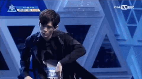 a man in a black suit is dancing on a stage with a mnet logo in the background .