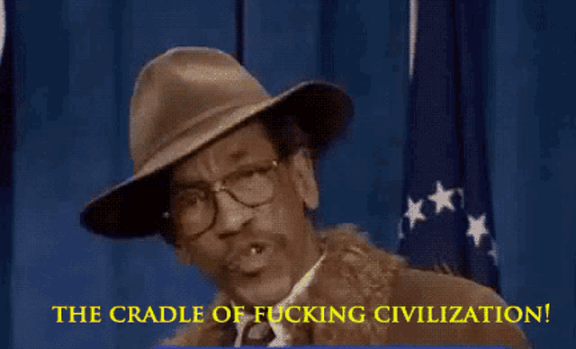 a man wearing a hat and glasses stands in front of a flag and says the cradle of fucking civilization