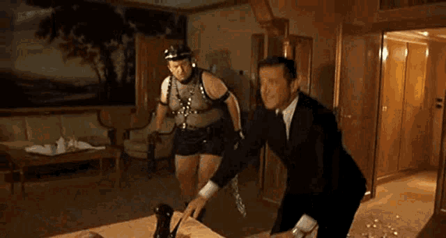 a man in a suit and tie is dancing in a living room with a painting on the wall .