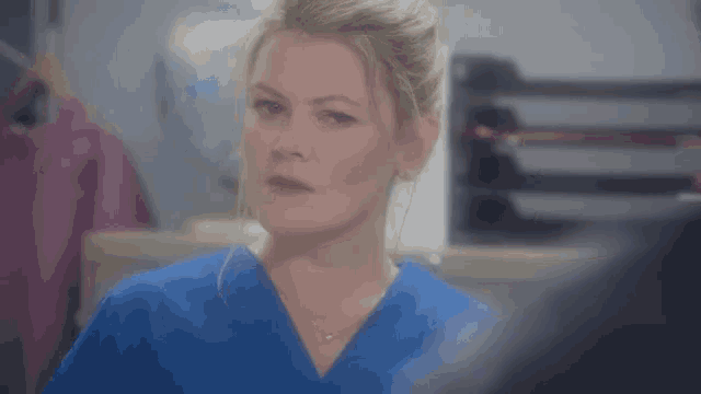 a woman in a blue scrub top is standing in a hospital room .
