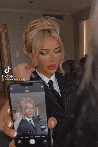 a woman in a suit and tie is taking a selfie
