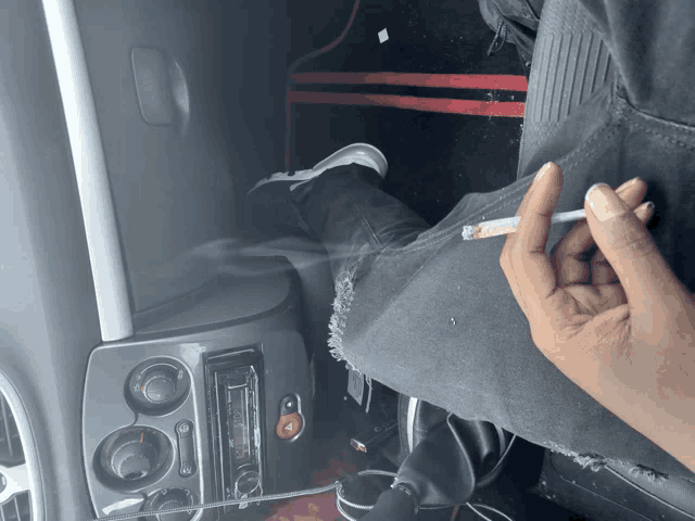 a person smoking a cigarette in a car with a pioneer radio in the background