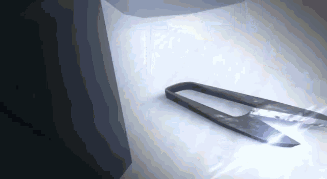 a pair of scissors is sitting on a white surface with a light shining on it .