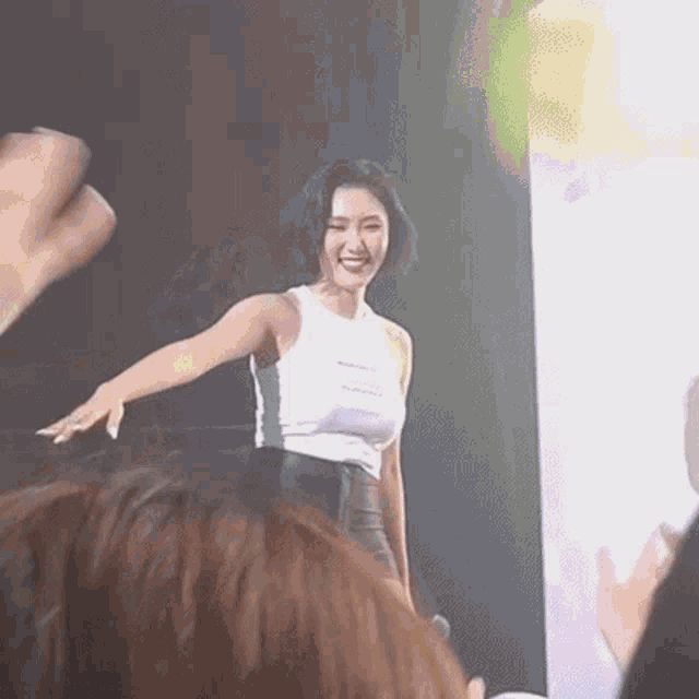 a woman in a white tank top is standing on a stage in front of a crowd of people .