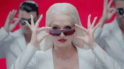 a woman wearing sunglasses is standing in front of a group of men .