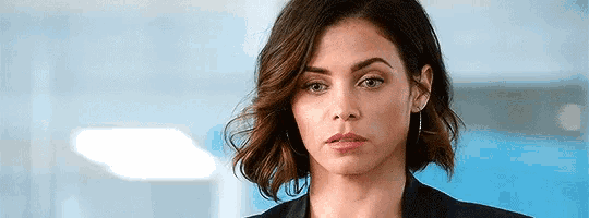 a woman with short hair is wearing a black jacket and earrings and making a serious face .