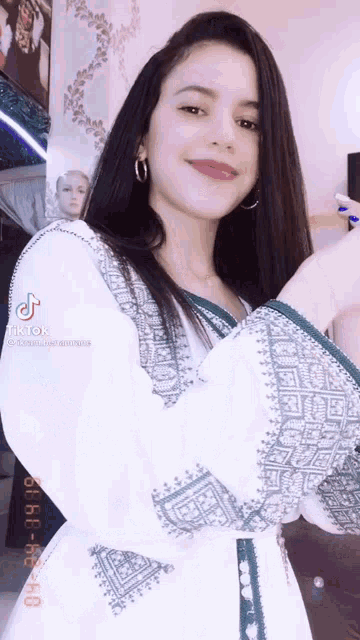 a young woman in a white dress with green embroidery is standing in front of a mannequin .