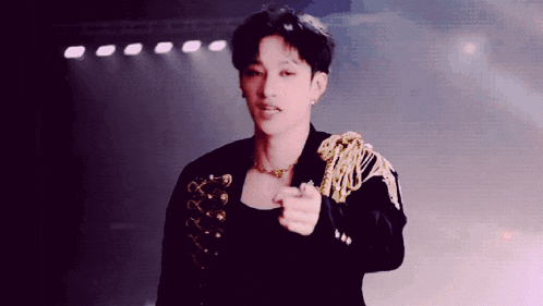 a young man wearing a black jacket and gold shoulder pads is pointing at the camera