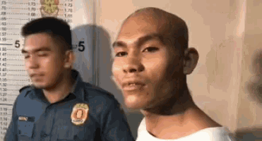 a man with a bald head is standing next to a police officer in front of a measuring tape .