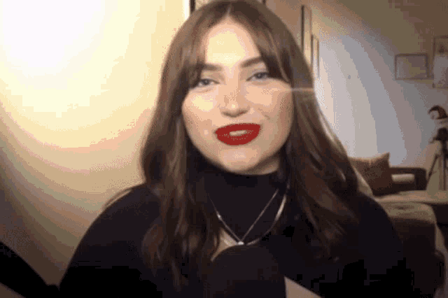 a woman wearing red lipstick and a black turtleneck is speaking into a microphone .