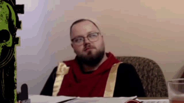 a man with a beard and glasses is sitting at a table with papers on it .