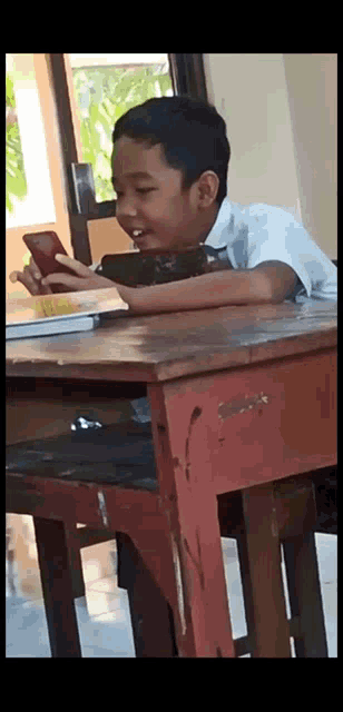 a boy is sitting at a desk looking at his phone
