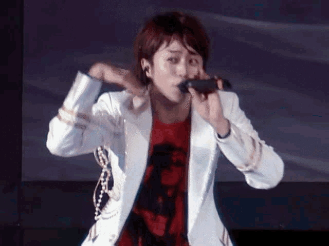 a man singing into a microphone while wearing a white jacket