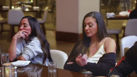 two women are sitting at a table in a restaurant looking at their cell phones .