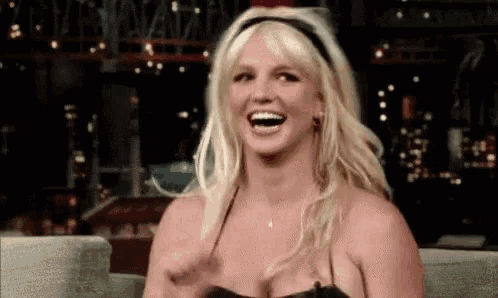 britney spears is laughing while sitting in a chair and wearing a headband .