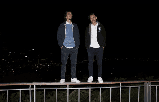 two men standing on top of a railing with one wearing a jacket that says ' california ' on it