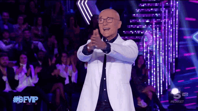 a bald man in a white jacket and glasses stands on a stage in front of a crowd and says #gfvip on the bottom