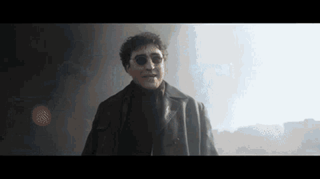 a man in a black coat and sunglasses is standing in a dark room .