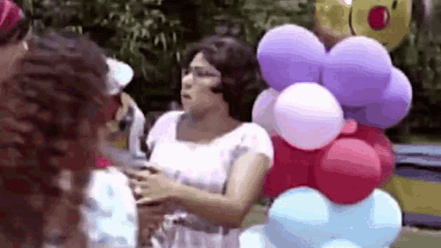 a woman in a white dress is standing in front of a bunch of colorful balloons .